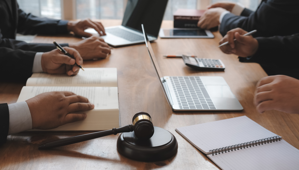 A group of lawyers are gathered at a table with laptops, notebooks and a calculator.