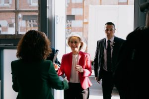 Ursula von der Leyen arrives at the European Employment and Social Rights Forum 2026 walking through a door and holding her hands out to greet someone. She wears a white shirt and pink jacket